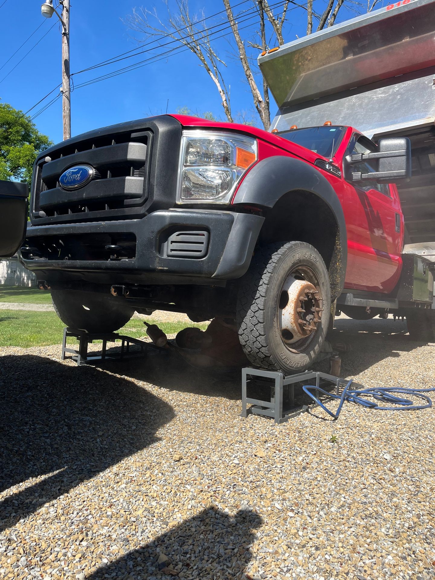 Red truck elevated on metal stands with a person working underneath in a sunny outdoor area.